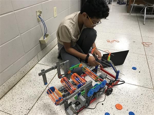 A student sits with their robot to work on it at practice.